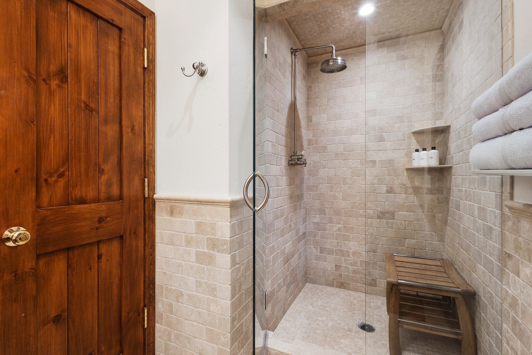 A shower with a glass door, a wooden bench, and a towel rack.