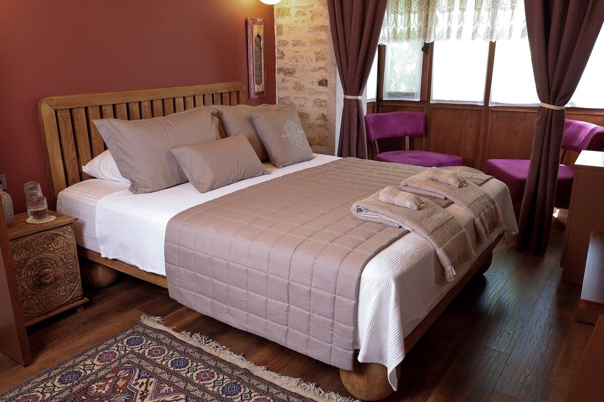 Una cama bien hecha con cabecera de madera, una alfombra estampada y una mesita de noche con un adorno.