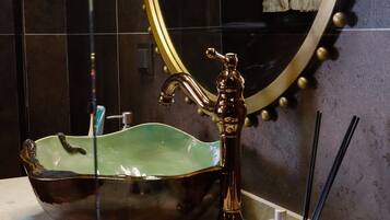 Un baño con un espejo ovalado grande, un lavabo de cerámica verde y un grifo dorado.