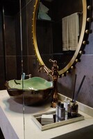 Un baño con un espejo ovalado grande, un lavabo de cerámica verde y un grifo dorado.