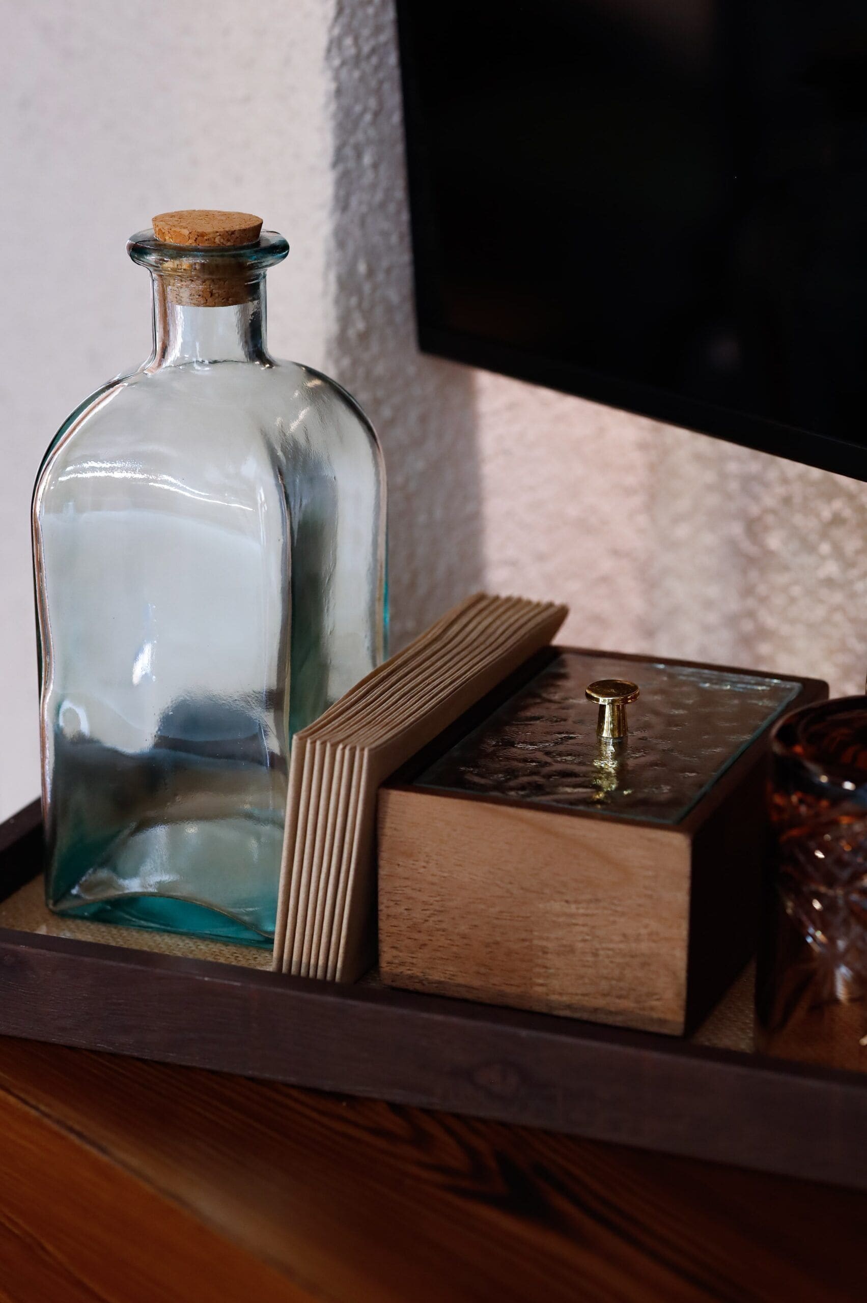 A clear glass bottle with a cork stopper on a wooden tray.