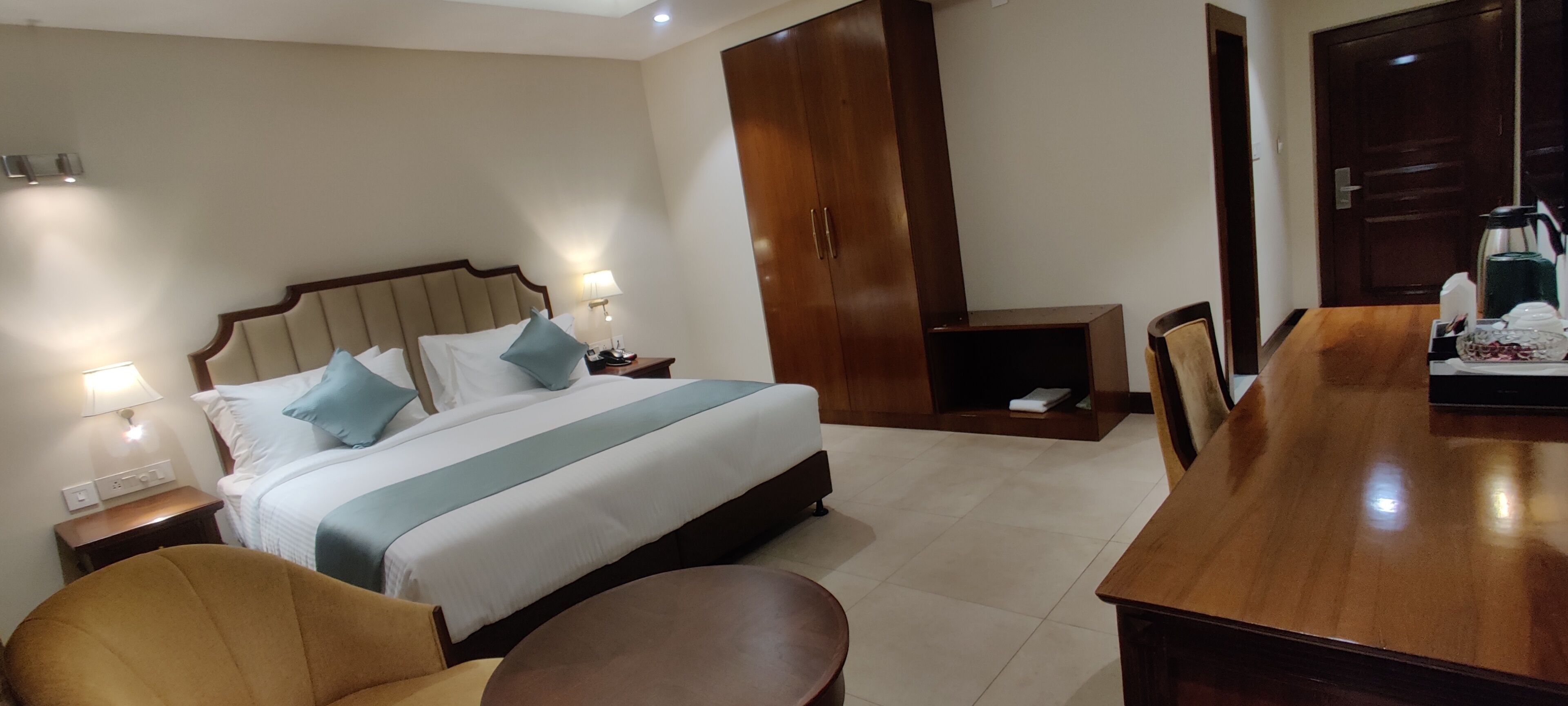 Una habitación de hotel con cama, mesitas de noche, armario de madera, mesa de comedor y una silla.