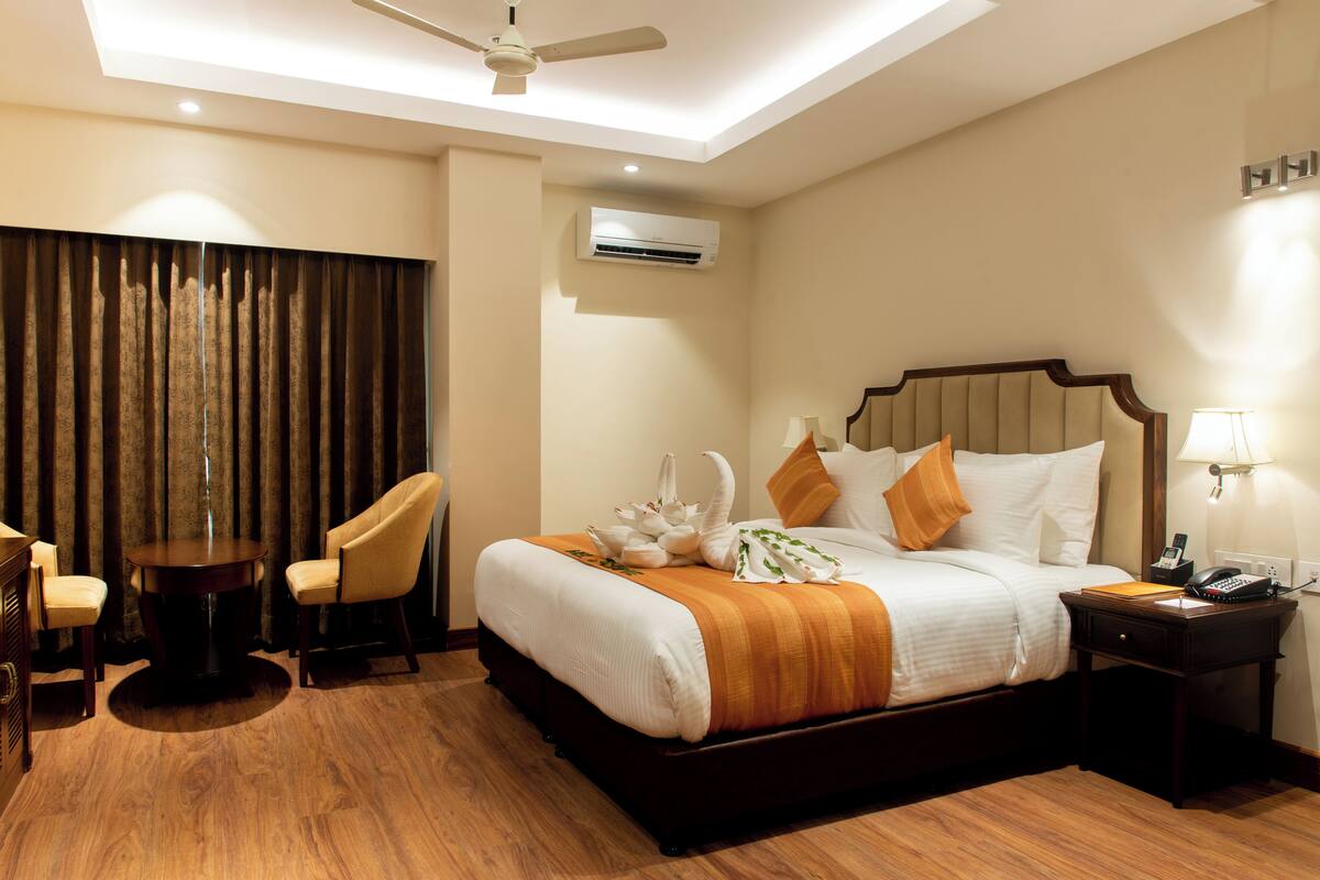 Quarto de hotel com cama, escrivaninha, cadeira, mesa, ar condicionado e ventoinha no teto.