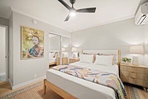 Ein Schlafzimmer mit einem Bett, Nachttischen, einem Deckenventilator und einer Wand-Klimaanlage.