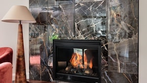 A modern living room with a fireplace, a flat-screen TV mounted above it, and a red armchair. - Luxury Poconos Estate*Golf Sim*Pickleball*Sauna (Long Pond)
