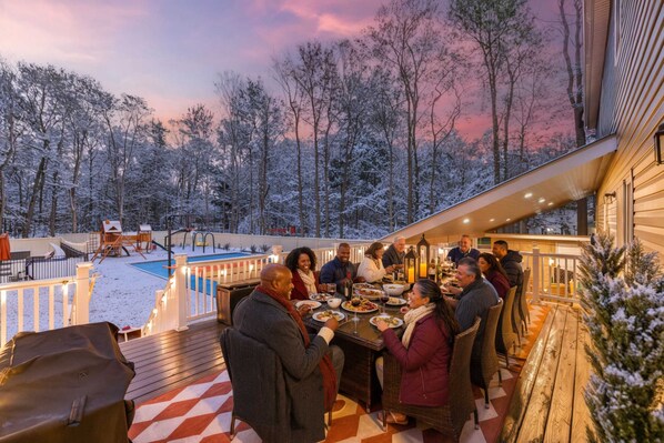 A group of people dining outdoors on a deck with a pool in the background.