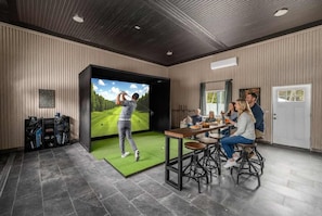 Una habitación moderna con equipo de simulación de golf, un comedor y una puerta con ventana.
