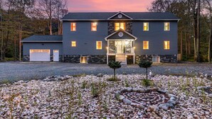 A two-story house with a stone facade, a front porch, and a driveway with a circular stone pattern. - Luxury Poconos Estate*Golf Sim*Pickleball*Sauna (Long Pond)