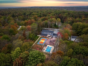 Eine Luftaufnahme eines Anwesens mit Schwimmbad, überdachter Terrasse und großem Haus, umgeben von dichtem Wald.