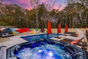 Un bain à remous avec une piscine, un espace salon extérieur et une fresque murale en arrière-plan.