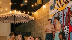 Un espace piscine où les gens se détendent, une fresque murale avec le mot « Bienvenue » et des guirlandes lumineuses.
