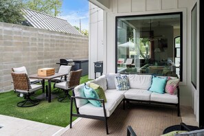 A patio with a white sofa, two chairs, a table, and a barbecue grill.