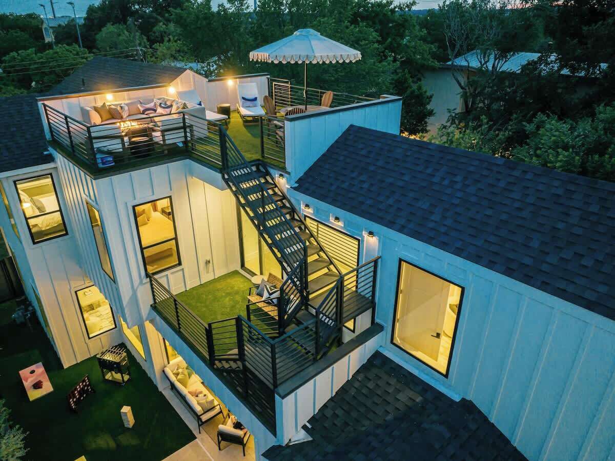 A modern two-story house with a balcony, outdoor seating, and a staircase.