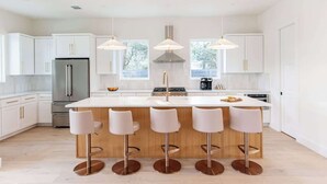 Une cuisine moderne avec des meubles blancs, un îlot central doté de tabourets, des appareils en acier inoxydable et un éclairage suspendu.