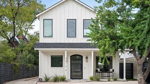 Une maison à deux étages avec un porche à l’avant, une porte noire et un petit patio.