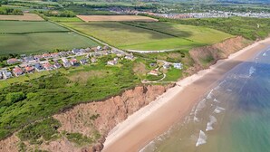 An aerial view of a coastal area with a beach, houses, and fields. - Shoe Buttons Cottage at Gap Road (Filey)