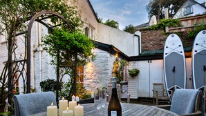 Une terrasse extérieure avec une table en bois dressée pour un repas, entourée de bougies et d’une bouteille de vin.