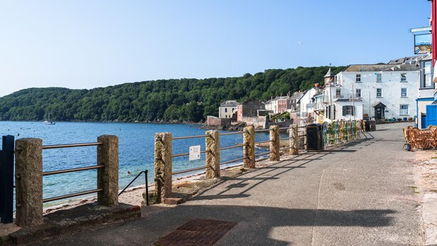 A coastal road with stone railings, buildings, and a body of water. - Roselric (Kingsand)