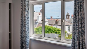 A room with a large window, curtains, and a view of buildings and a clock tower. - Roselric (Kingsand)