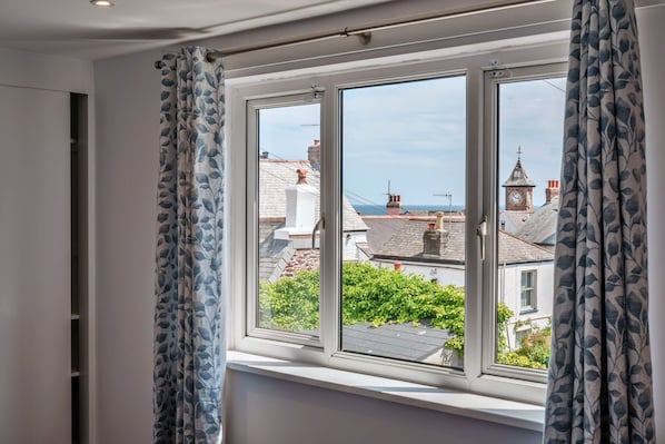 A room with a large window, curtains, and a view of buildings and a clock tower.