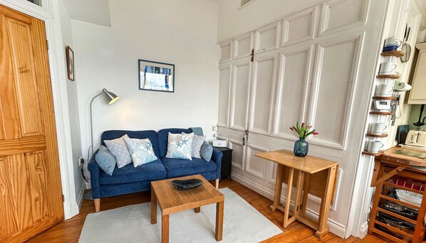 A living room with a blue sofa, a small wooden table, and a white cabinet with shelves. - The Wash House, Kingsand (Kingsand)