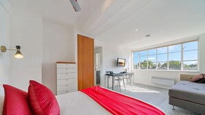 A modern bedroom with a bed, a desk, and a view of the city.