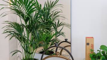 Una habitación moderna con un espejo grande, una planta en maceta verde, una planta en maceta azul y una caja de cartón sobre un mueble blanco.