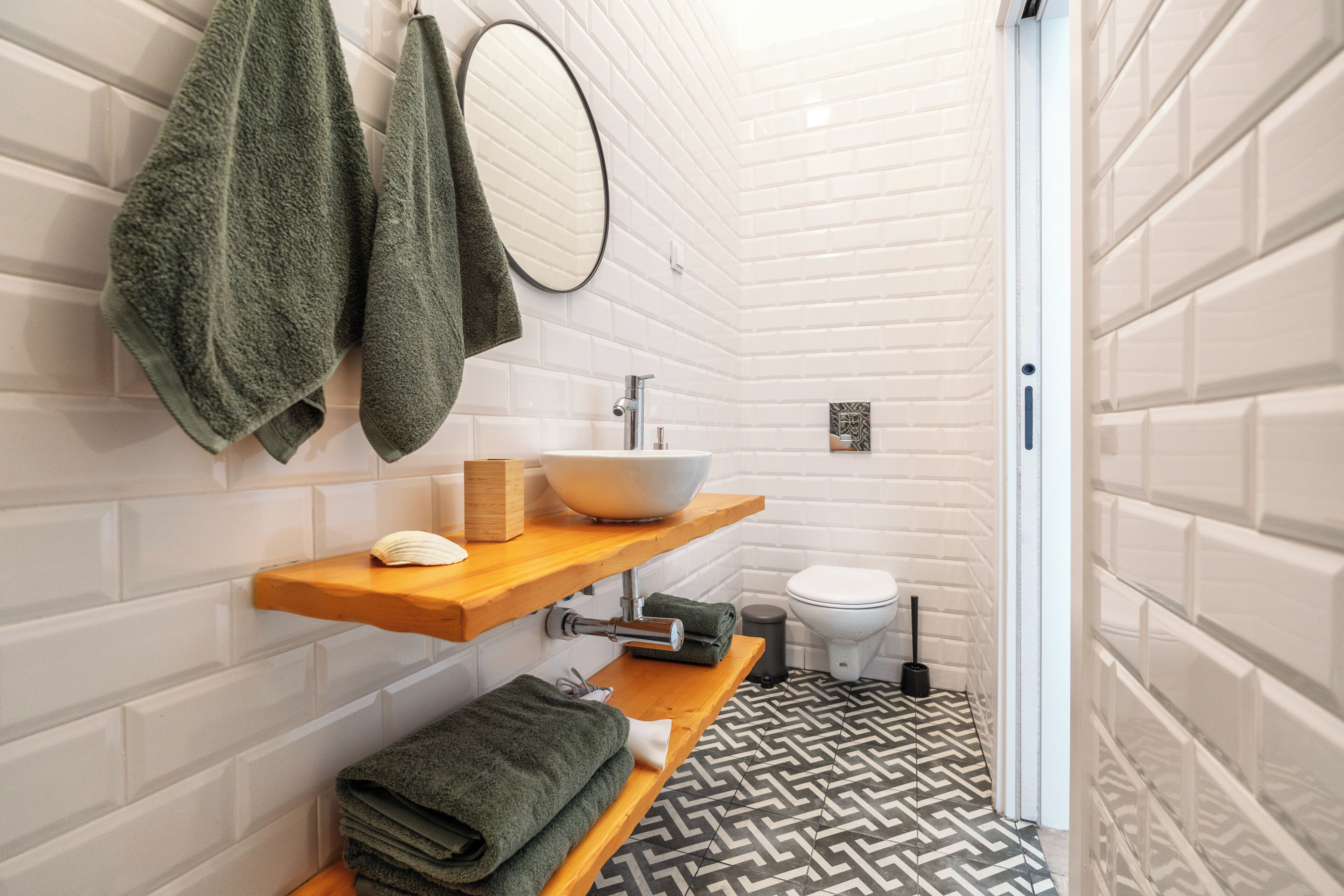 Un baño con paredes de azulejos blancos, un lavamanos blanco y un suelo con diseño en blanco y negro.