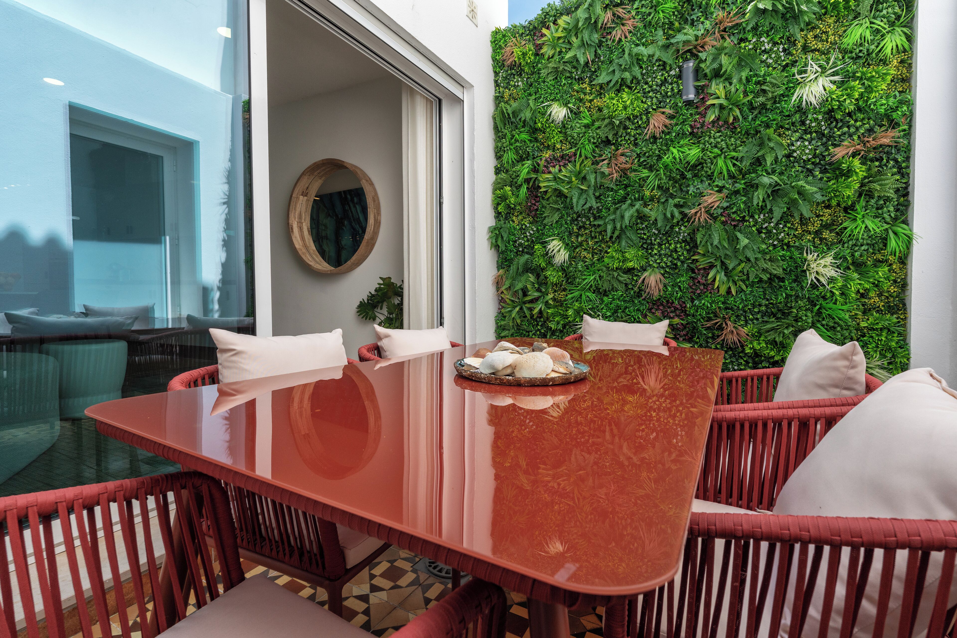 A dining area with a glass table, red wicker chairs, and a green vertical garden wall.