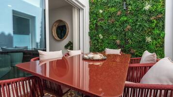 A dining area with a glass table, red wicker chairs, and a green vertical garden wall.