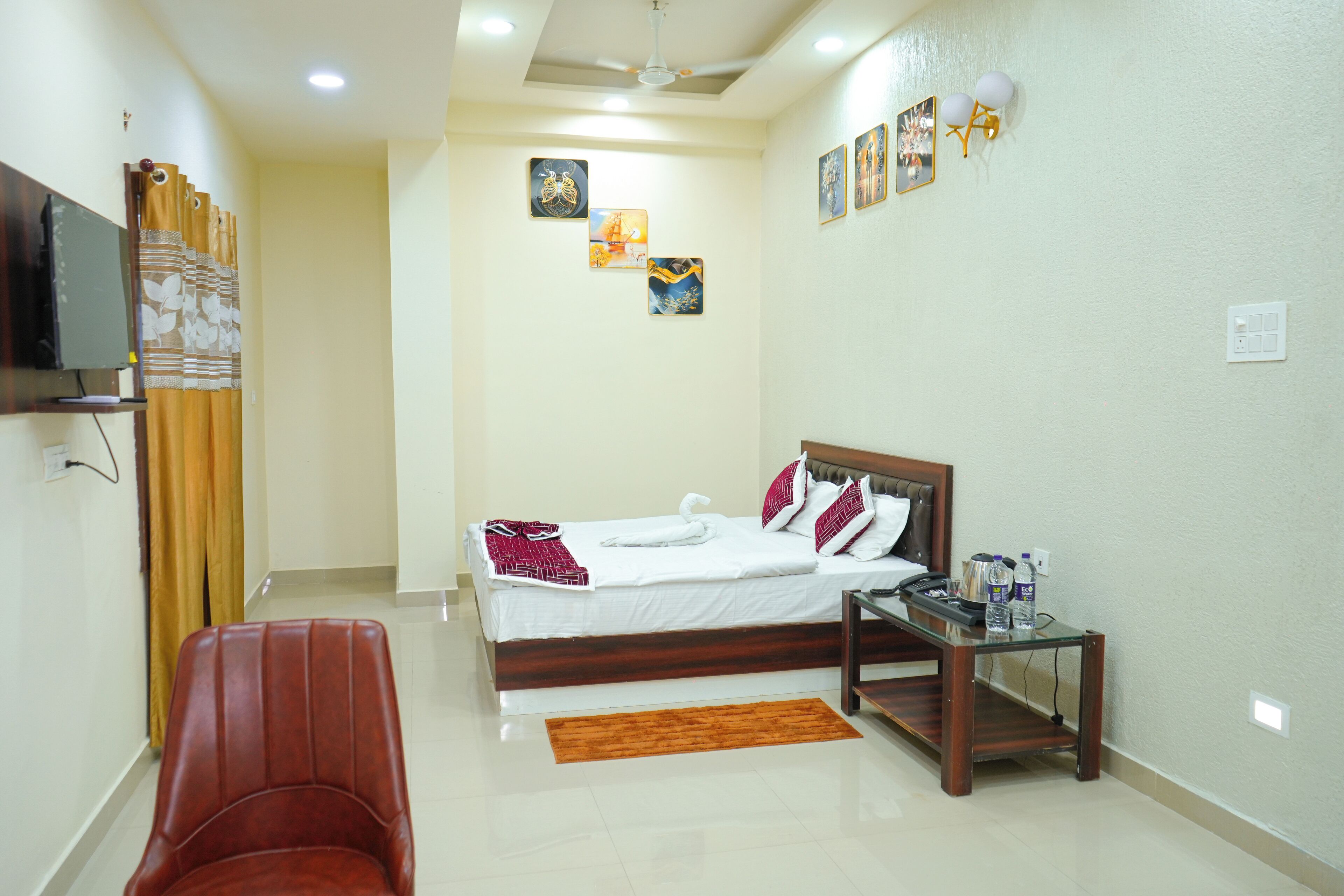 A hotel room with a bed, a chair, a small table, and artwork on the walls.