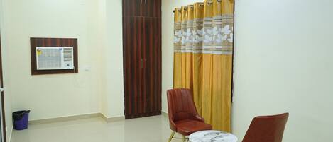 A room with a wardrobe, a curtain, two chairs, and a small table.
