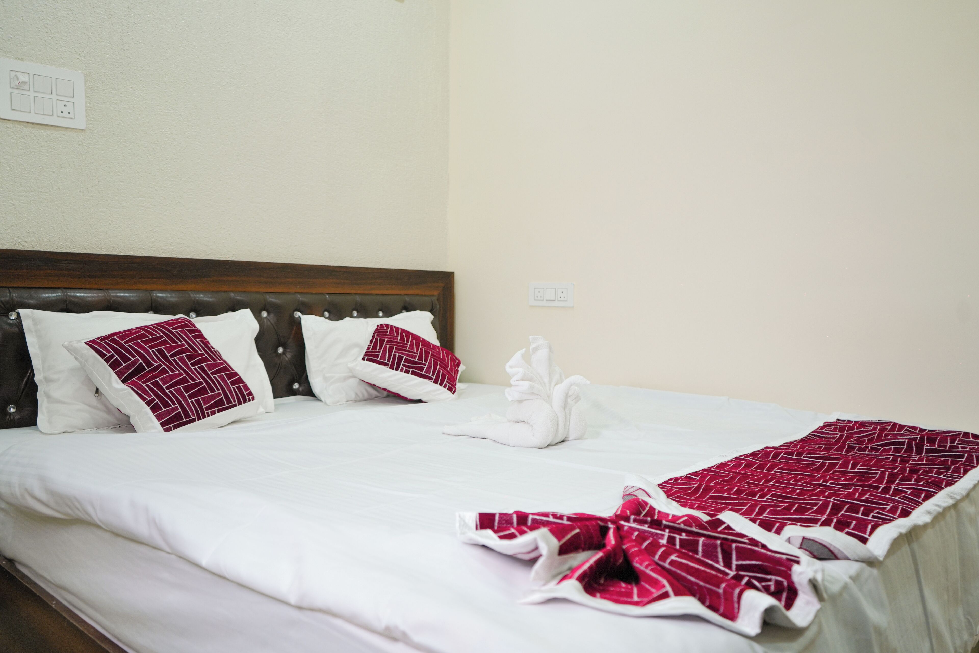 A neatly made bed with white bedding and red patterned pillows, a wooden headboard, and a red and white patterned throw blanket.