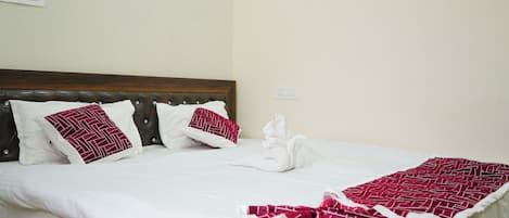 Una cama bien tendida con ropa blanca y almohadas estampadas en rojo, un cabecero de madera y una manta con estampado rojo y blanco.