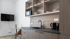 Una cocina moderna con microondas integrado, cafetera negra y televisor de pantalla plana montado en la pared.