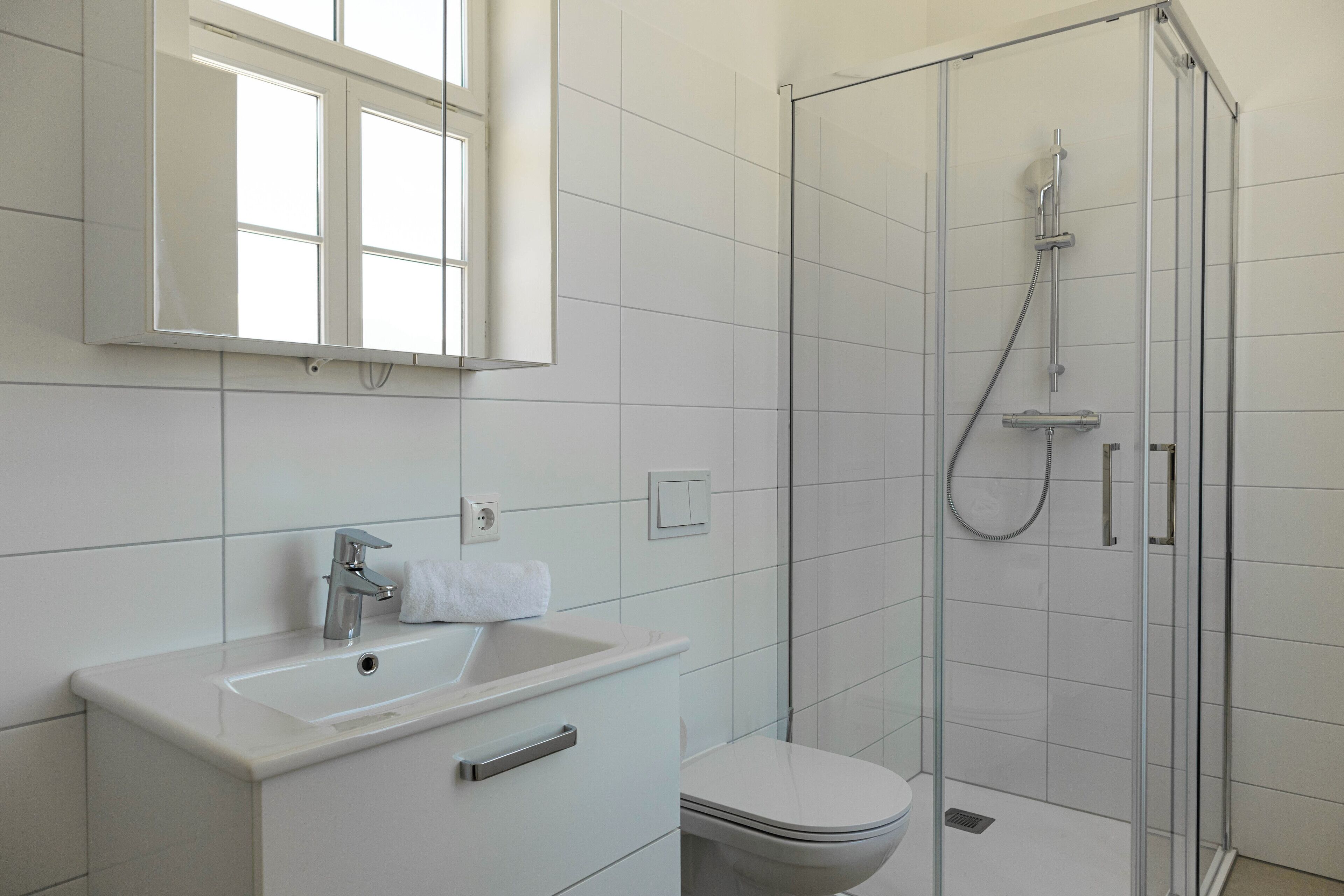 Ein modernes Badezimmer mit einer gläsernen Dusche, einem weißen Waschbecken und einer Toilette.