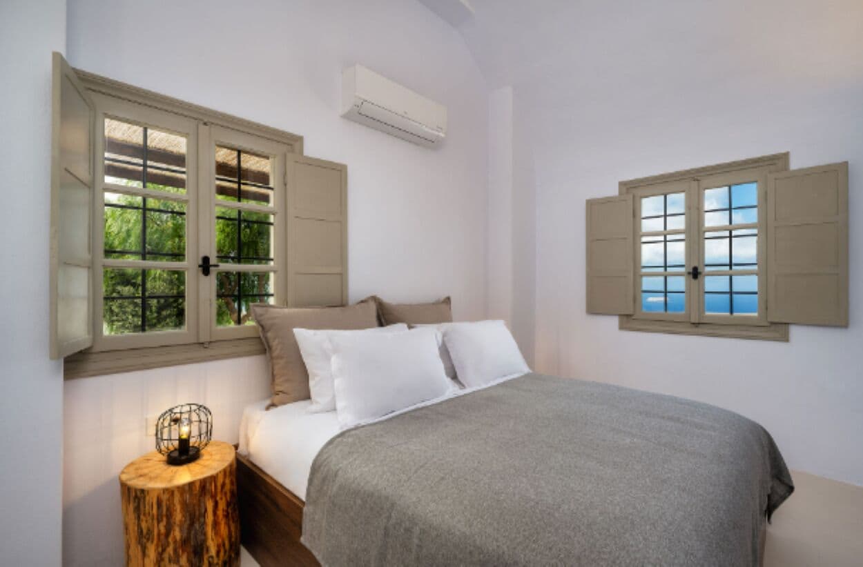 A bedroom with a bed, a nightstand, a window with shutters, and an air conditioning unit.