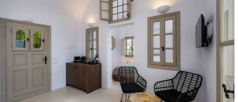 A modern interior with a wooden cabinet, two black wire chairs, a round wooden table, and a TV mounted on the wall.
