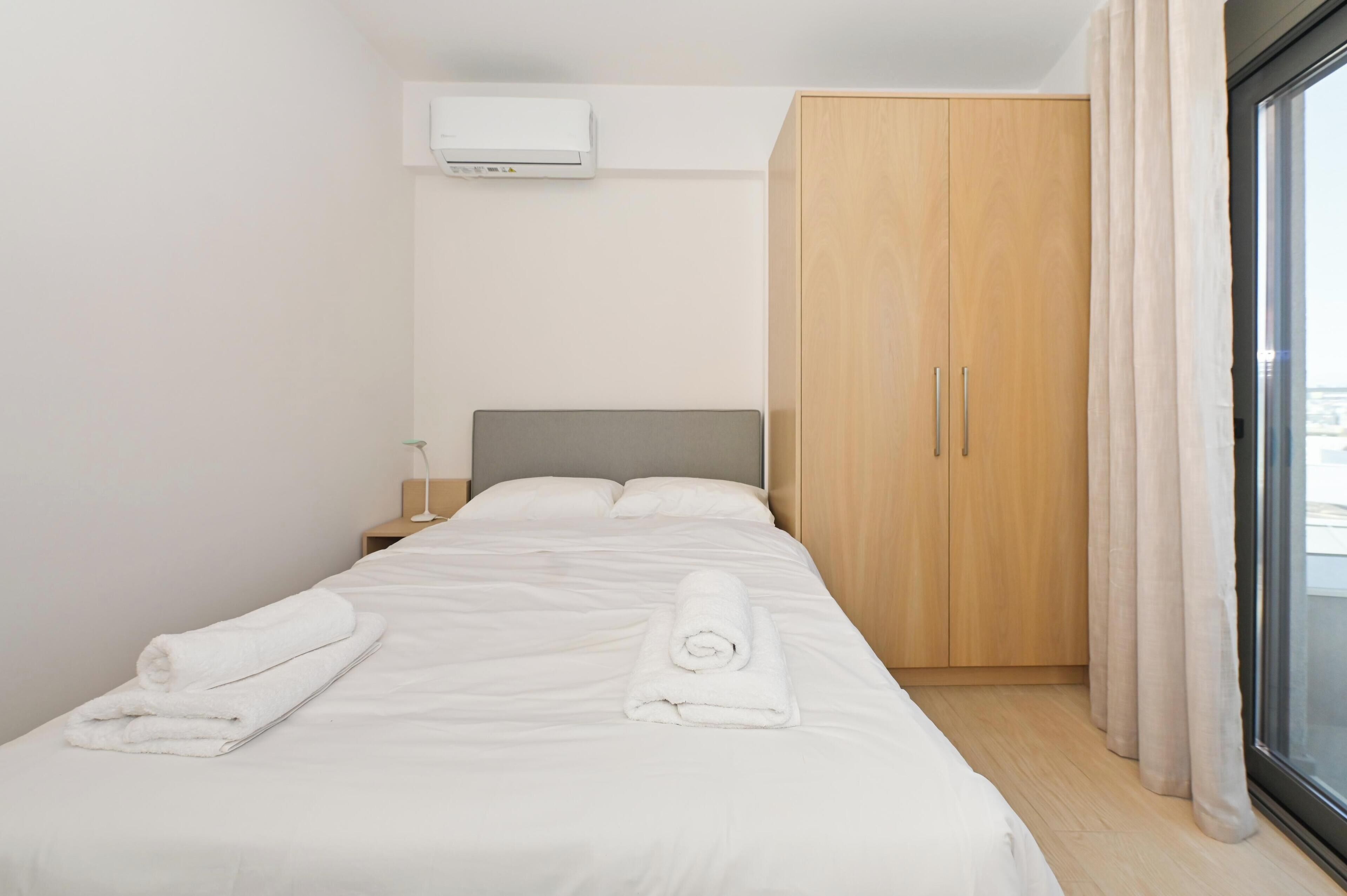 Quarto de hotel com cama, guarda-roupa, ar condicionado e janela com cortinas.