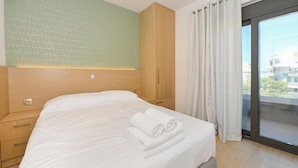 Een moderne hotelkamer met een groot bed, een houten garderobe en uitzicht op de stad door een groot raam.