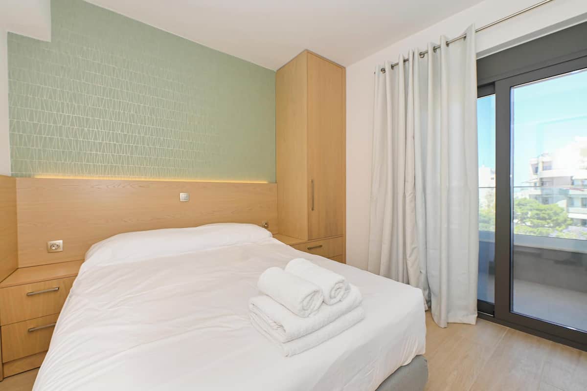 A modern hotel room with a large bed, a wooden wardrobe, and a view of the city through a large window.