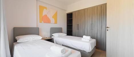 A hotel room with two beds, a wardrobe, and an air conditioning unit.