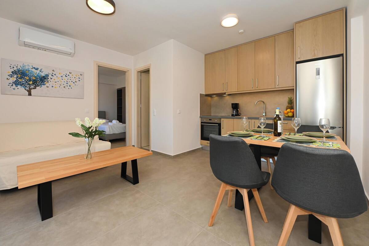A modern kitchen with wooden cabinets, a stainless steel refrigerator, and a dining area with a wooden table and chairs.