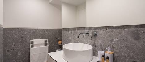 Un bagno moderno con un lavandino rotondo, un portascopevoli e uno specchio.