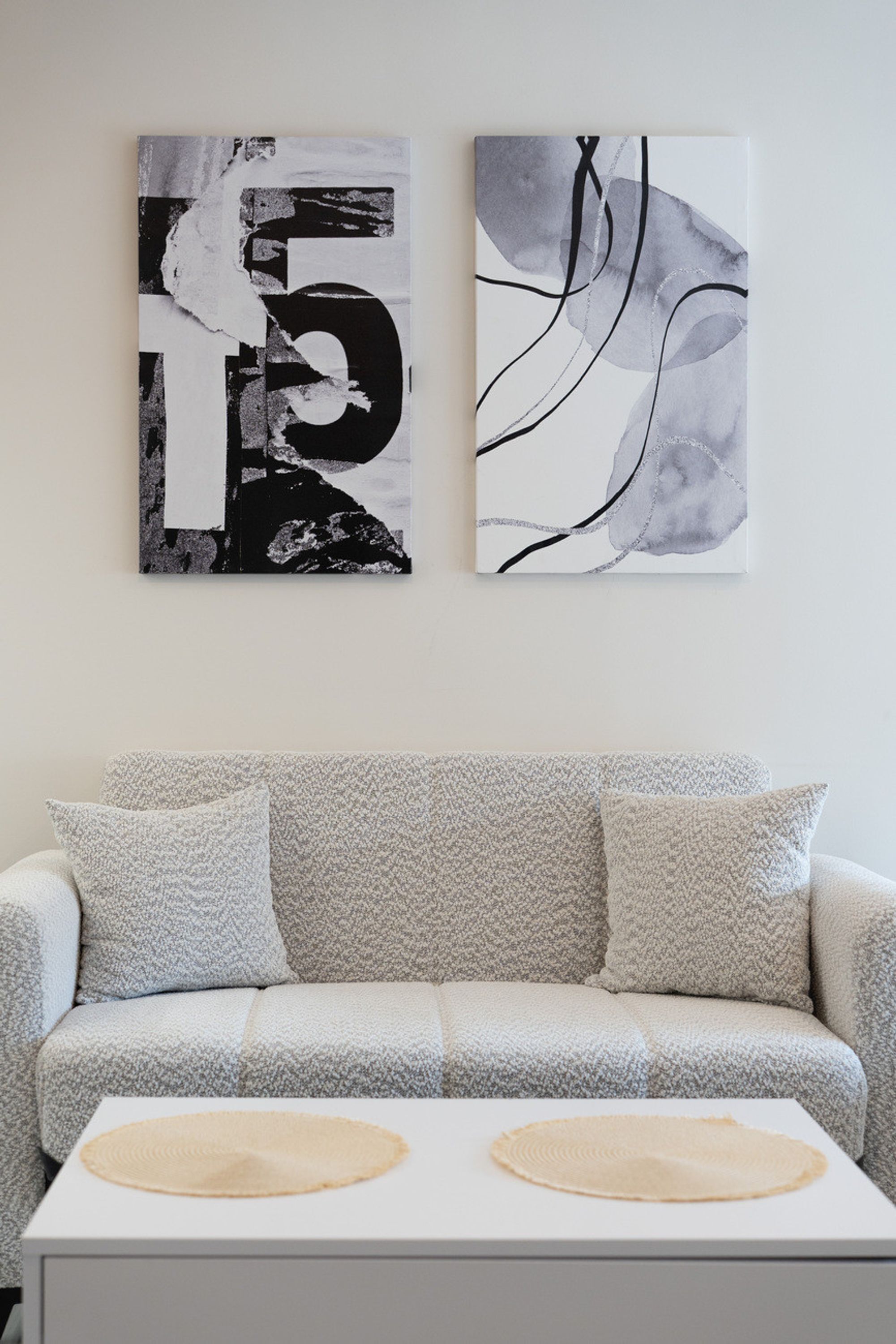 Una sala de estar moderna con un sofá gris, dos cuadros abstractos en la pared y una mesa de centro blanca con dos individuales.