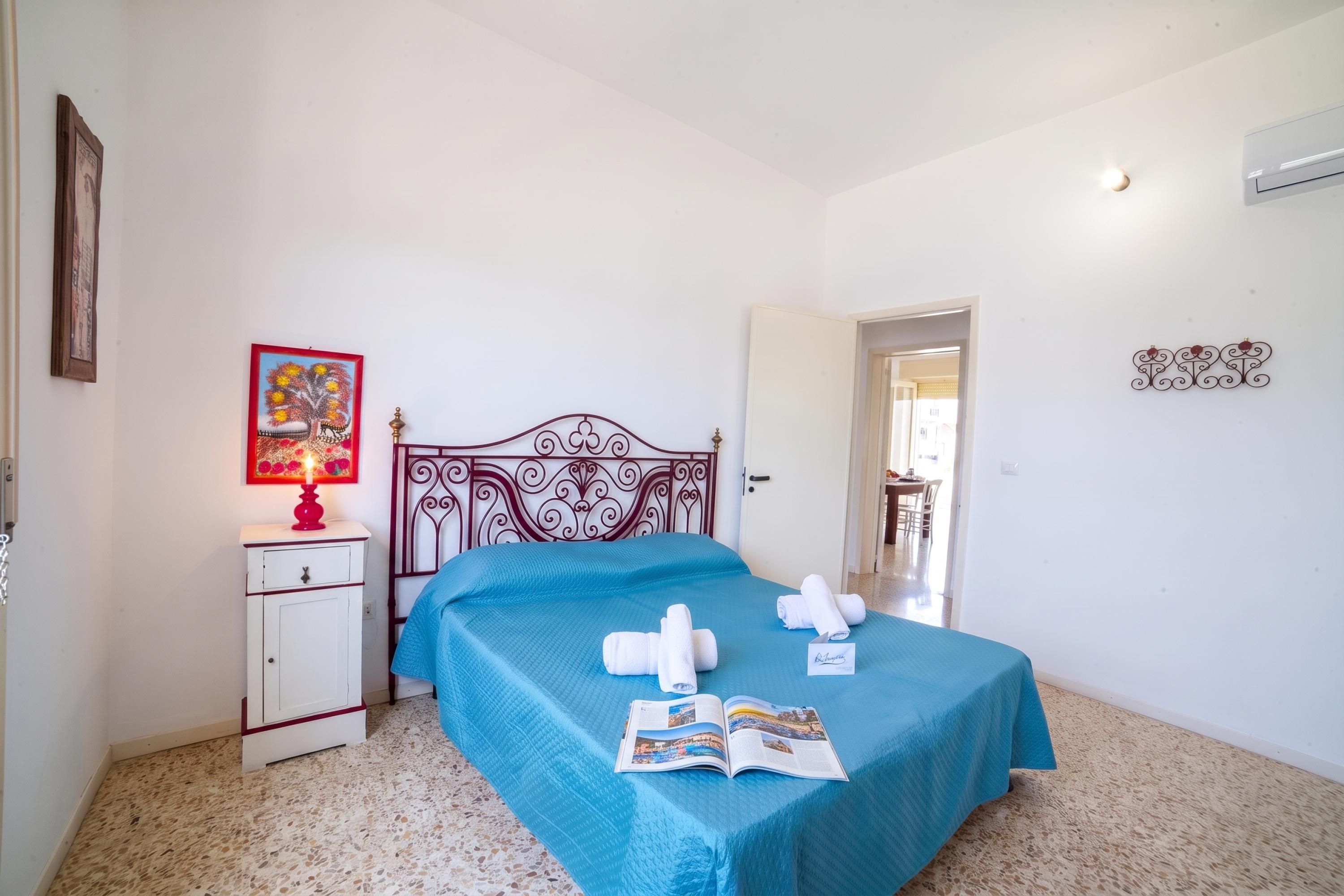 A bedroom with a bed, a nightstand, a lamp, and a door leading to another room.