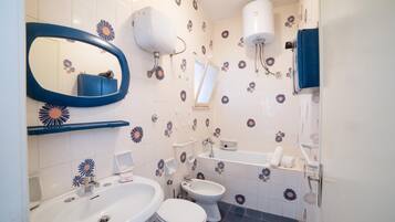 A bathroom with a sink, two toilets, a mirror, a towel rack, and a shower.