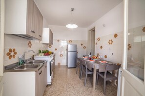 A modern kitchen with a stainless steel refrigerator, a sink, and a dining area set for four. - Giulia Sea View Villas (Santa Cesarea Terme)