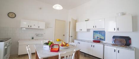 Una cocina con armarios blancos, una mesa de comedor con sillas, un reloj en la pared y un microondas en la encimera.