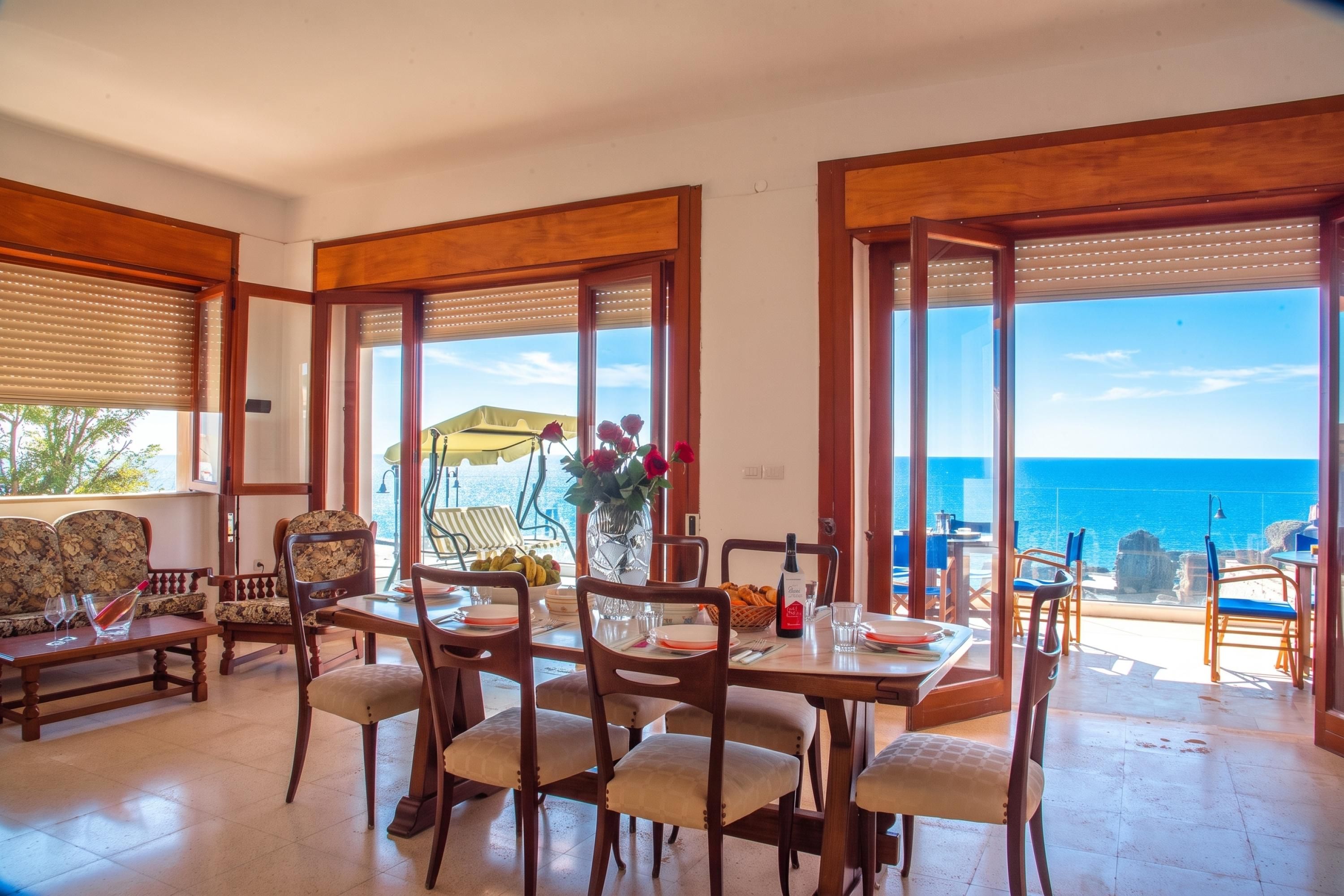 Un coin repas avec une table dressée pour quatre personnes, des chaises et une vue sur la mer.
